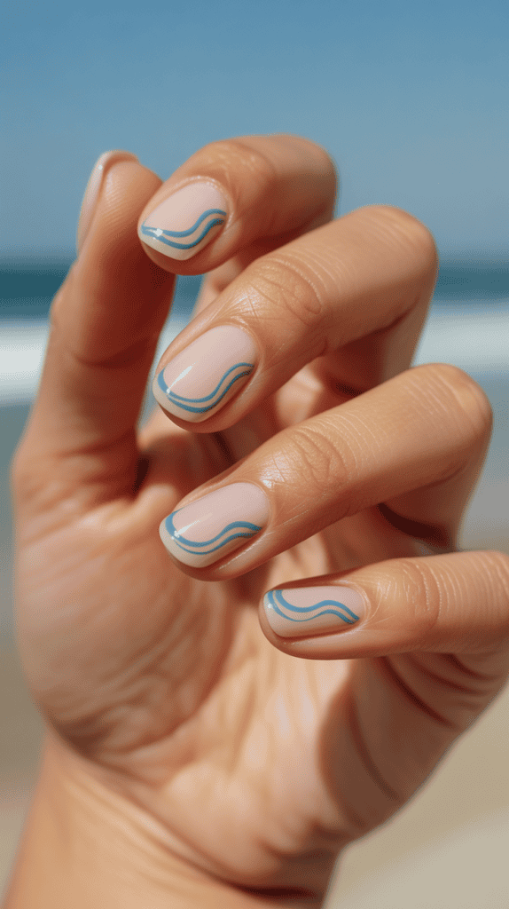 Hand showcasing beach-inspired nail art with blue wave designs on a sunny beach background.
