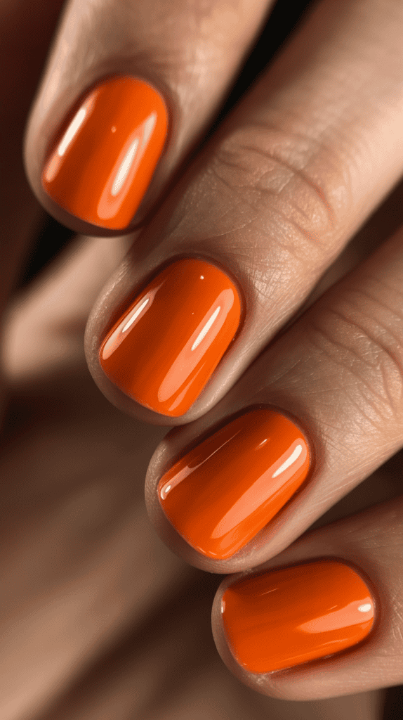 Bright orange nail polish on well-manicured nails, perfect for summer trends.