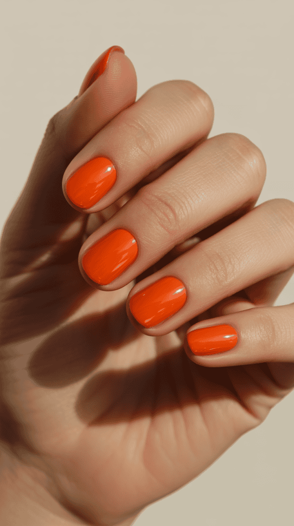 Bright orange nail polish on well-manicured nails, perfect for summer trends.