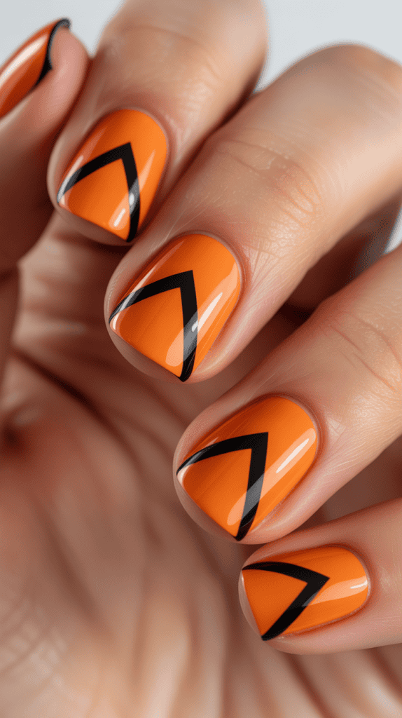 Bright orange nails with black geometric triangle designs for summer style.