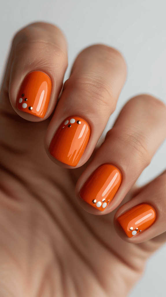 Close-up of bright orange summer nails with white and gold dot accents.