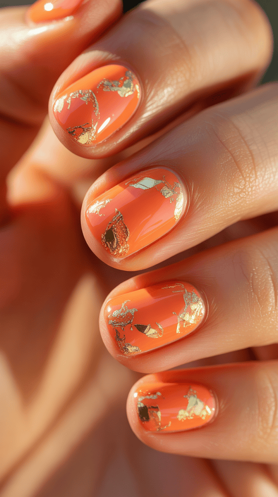 Bright orange summer nails with gold foil details, perfect for a chic and trendy look.